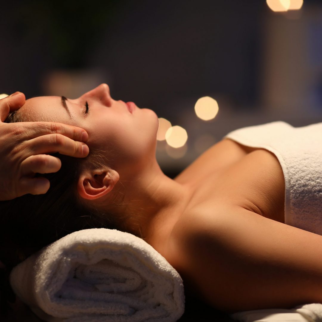 Woman lay on couch on her back with closed eyes and enjoy. Man make relaxing and therapeutic head massage at weight. Spa client has thrown her head back and rejuvenate. Wellness procedures in spa salon concept.